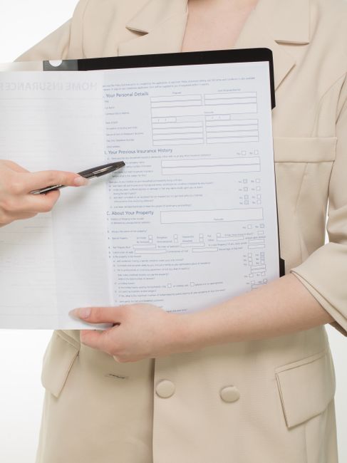 A close-up view of a home insurance policy form titled 'Home Insurance Policy', positioned on a desk or table next to a black pen and a small spiral-bound notebook, with other documents partially visi