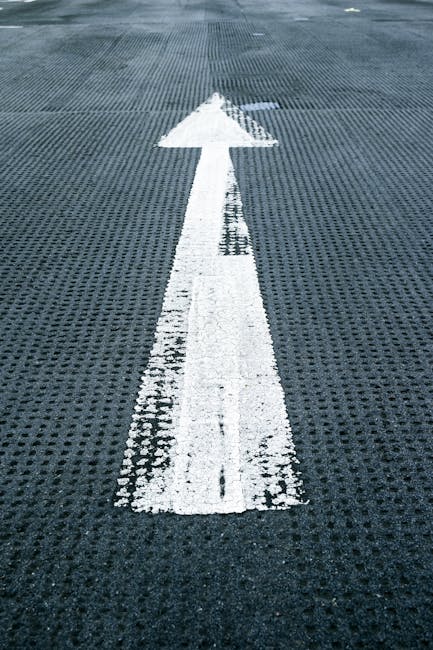 A white directional arrow painted on a textured, dark grey surface, likely a driveway or loading area outside a property, guiding the movement direction for vehicles or equipment used in house removal